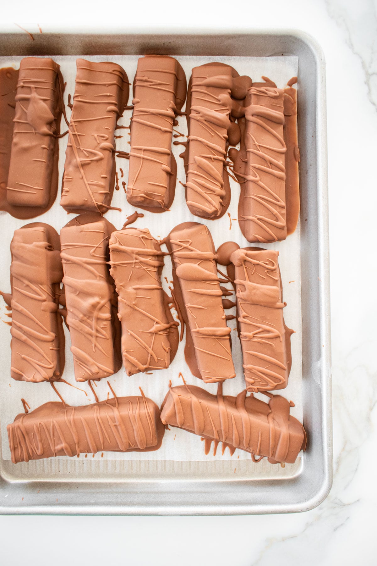 homemade twix bars on a baking sheet on a marble counter.