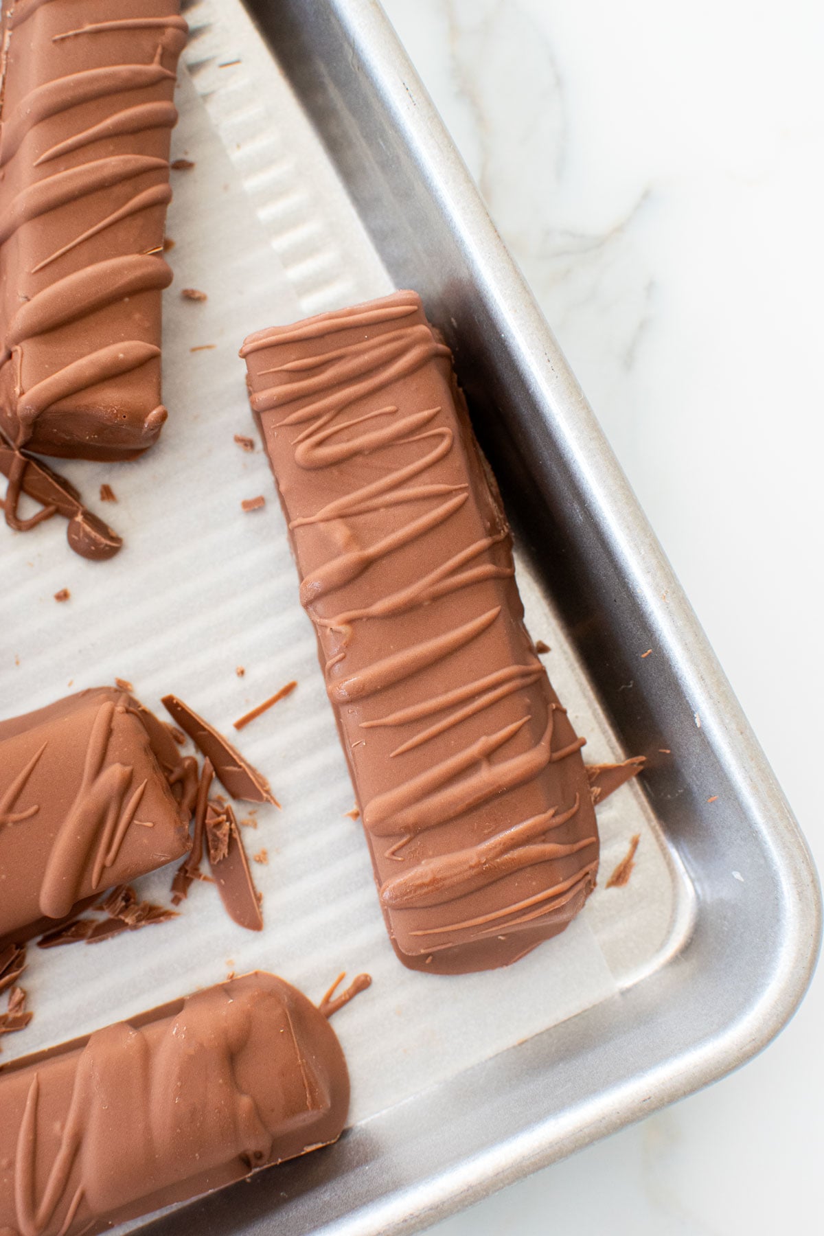 homemade twix bars on a baking sheet on a marble counter.