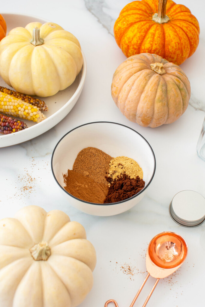 pumpkin pie spice mix spices in a bowl on a white marble counter with pumpkins.