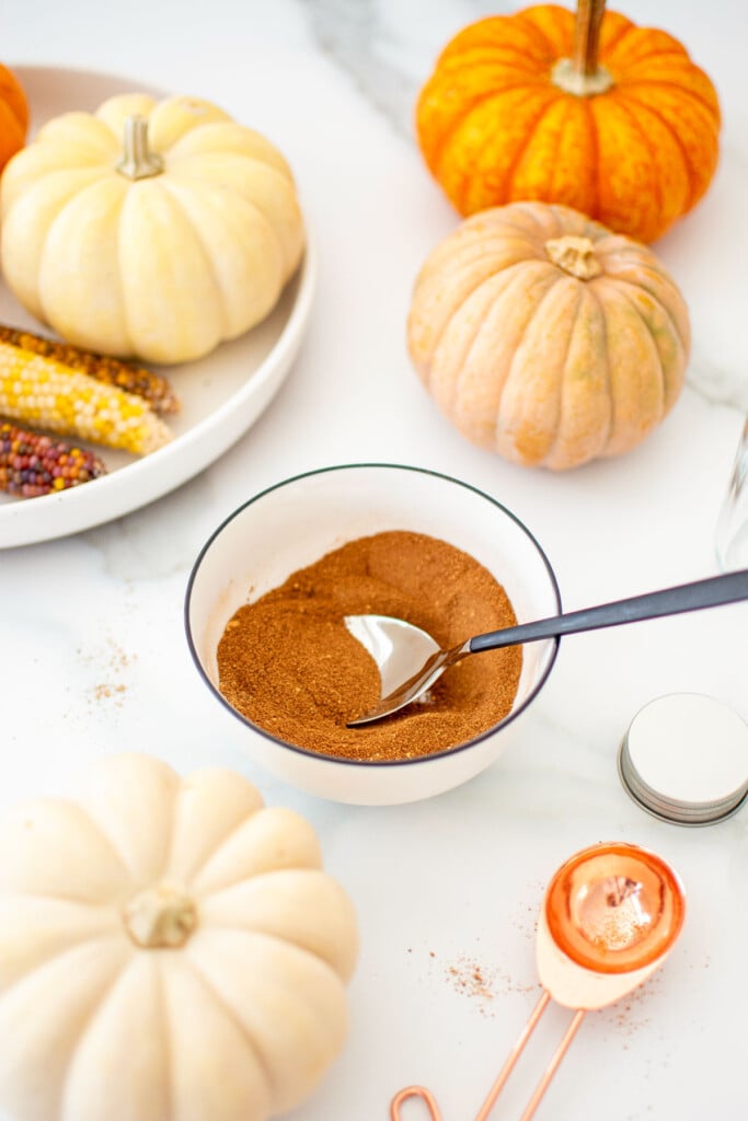 mixed pumpkin pie spice mix in a bowl on a white marble counter with pumpkins.