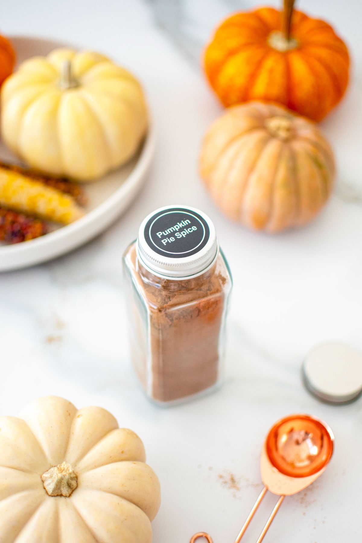 homemade pumpkin pie spice mix jar on a white marble counter with pumpkins.