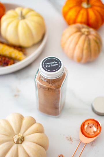 homemade pumpkin pie spice mix jar on a white marble counter with pumpkins.