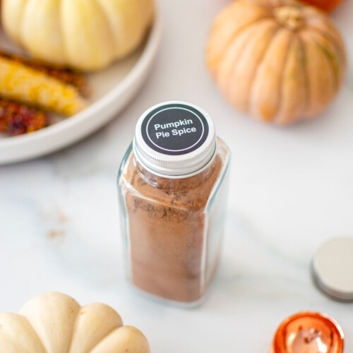 homemade pumpkin pie spice mix jar on a white marble counter with pumpkins.