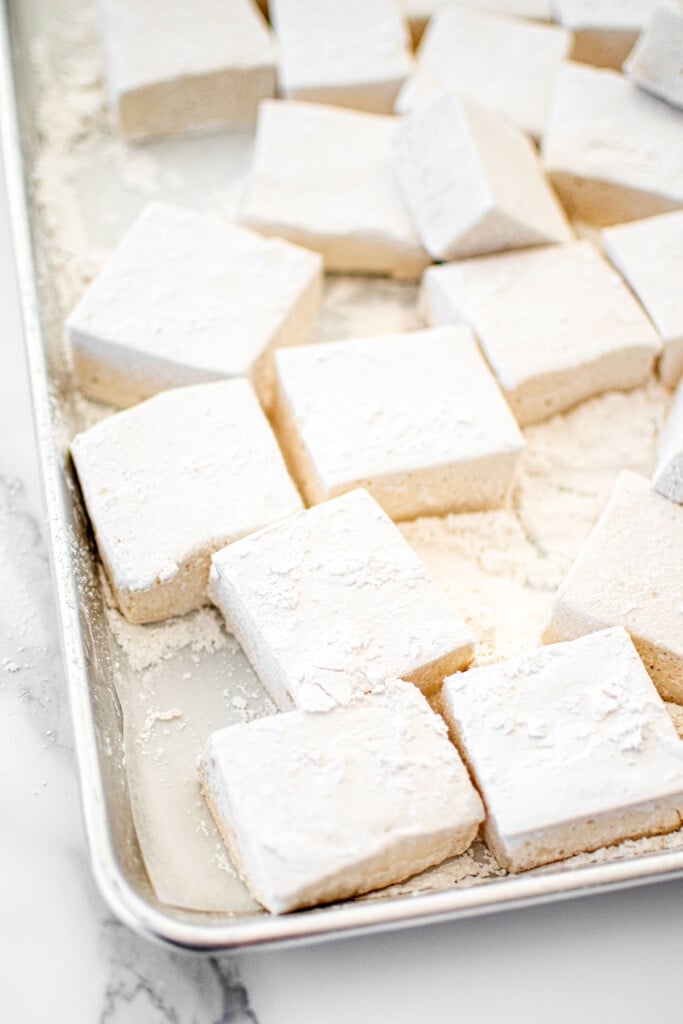 homemade marshmallows without eggs cut into large squares on a baking sheet on a white marble counter.