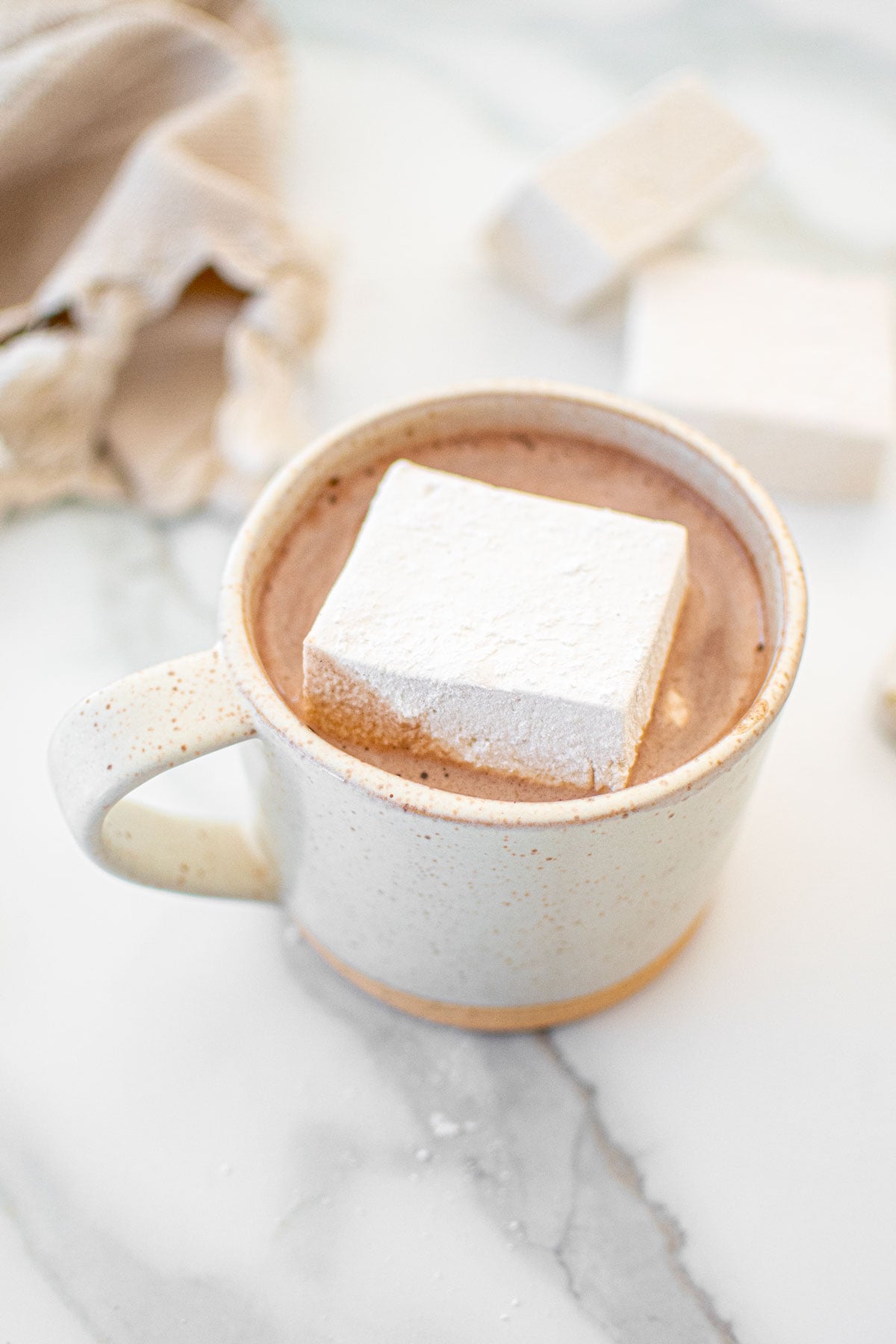 big homemade marshmallow in a mug of hot cocoa on a white marble counter.