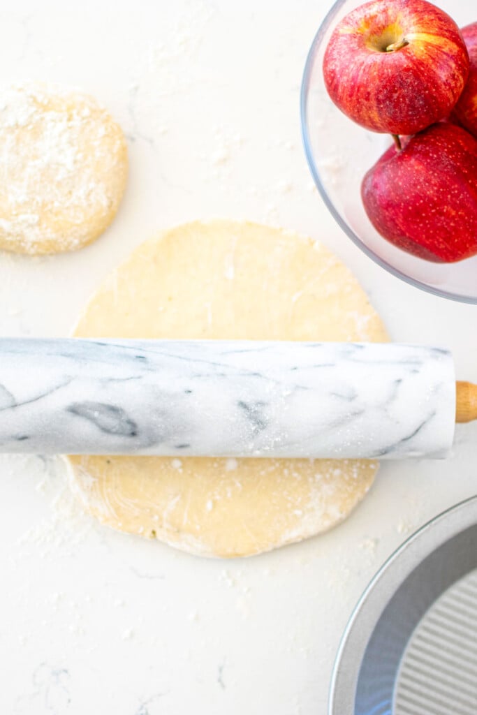 pie dough with a marble rolling pin on a white marble counter.