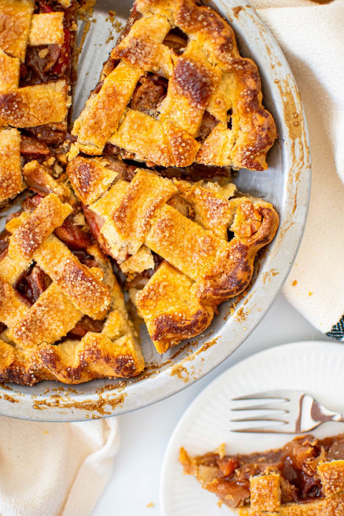 lattice spiced apple pie in a silver pie pan cut into slices on a white marble counter.