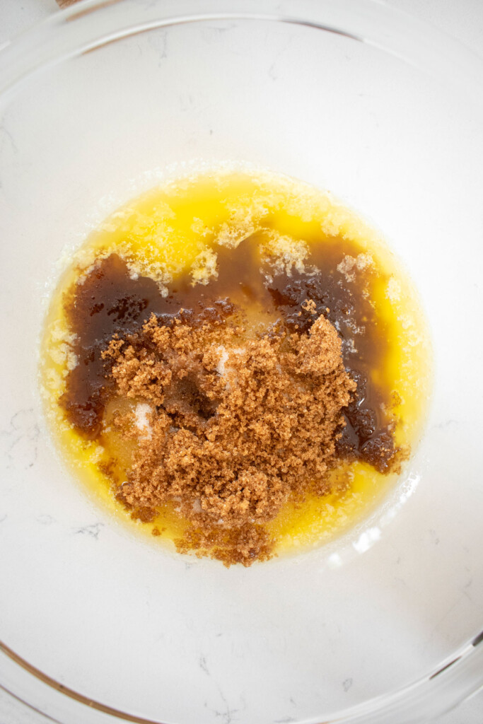 ingredients for pumpkin spice donut batter in a glass mixing bowl on a white marble counter.