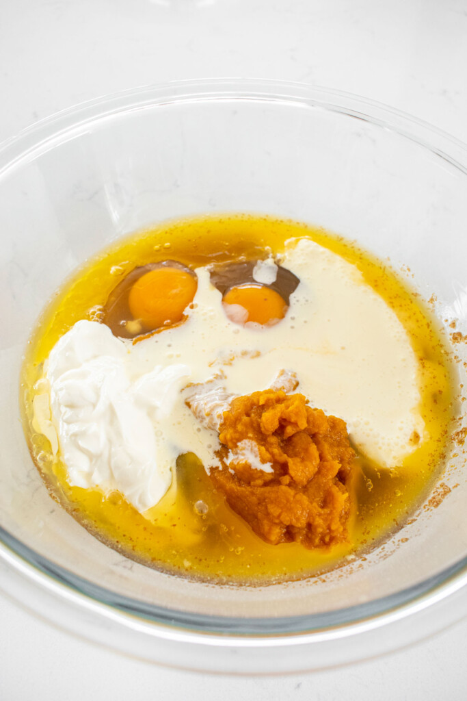 ingredients for pumpkin spice donut batter in a glass mixing bowl on a white marble counter.
