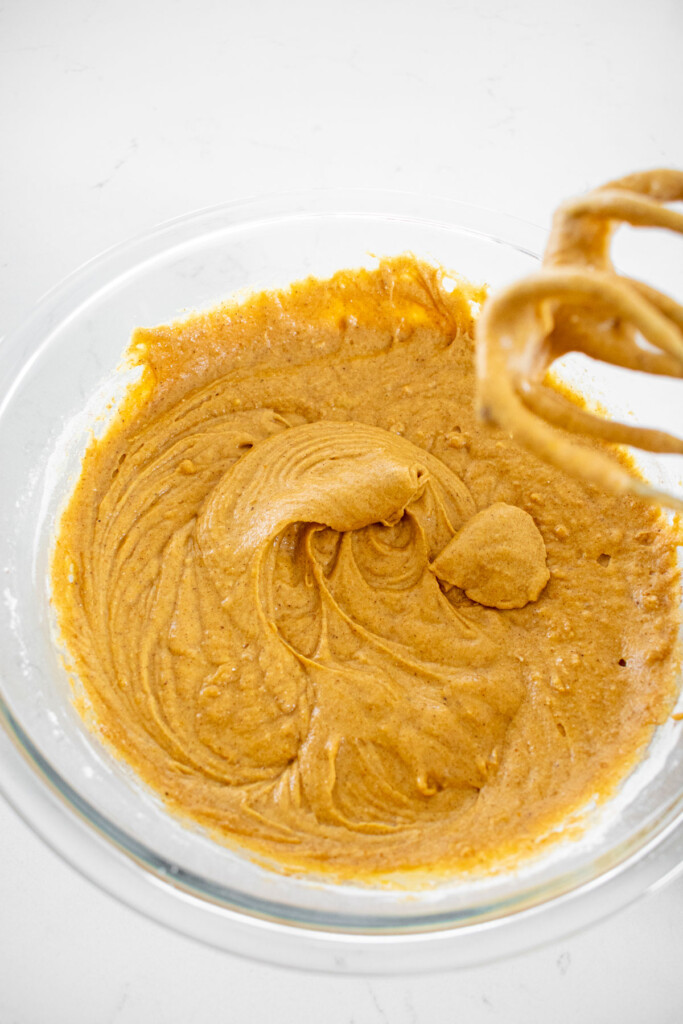pumpkin spice donut batter in a glass mixing bowl on a white marble counter.
