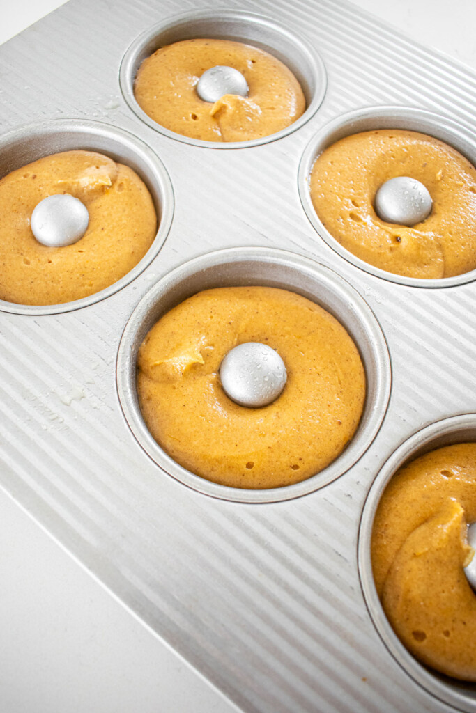 pumpkin spice donut batter in a donut pan on a white marble counter.