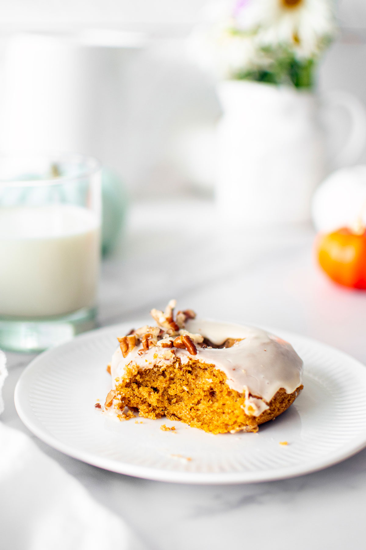 maple pumpkin spice donut with a bite taken out on a white plate on a white marble counter.