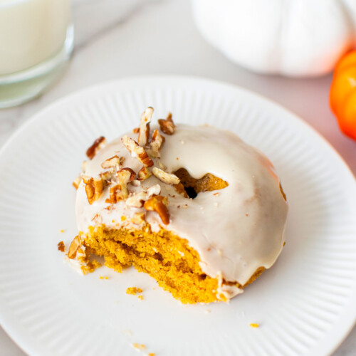 maple pumpkin spice donut with a bite taken out on a white plate on a white marble counter.