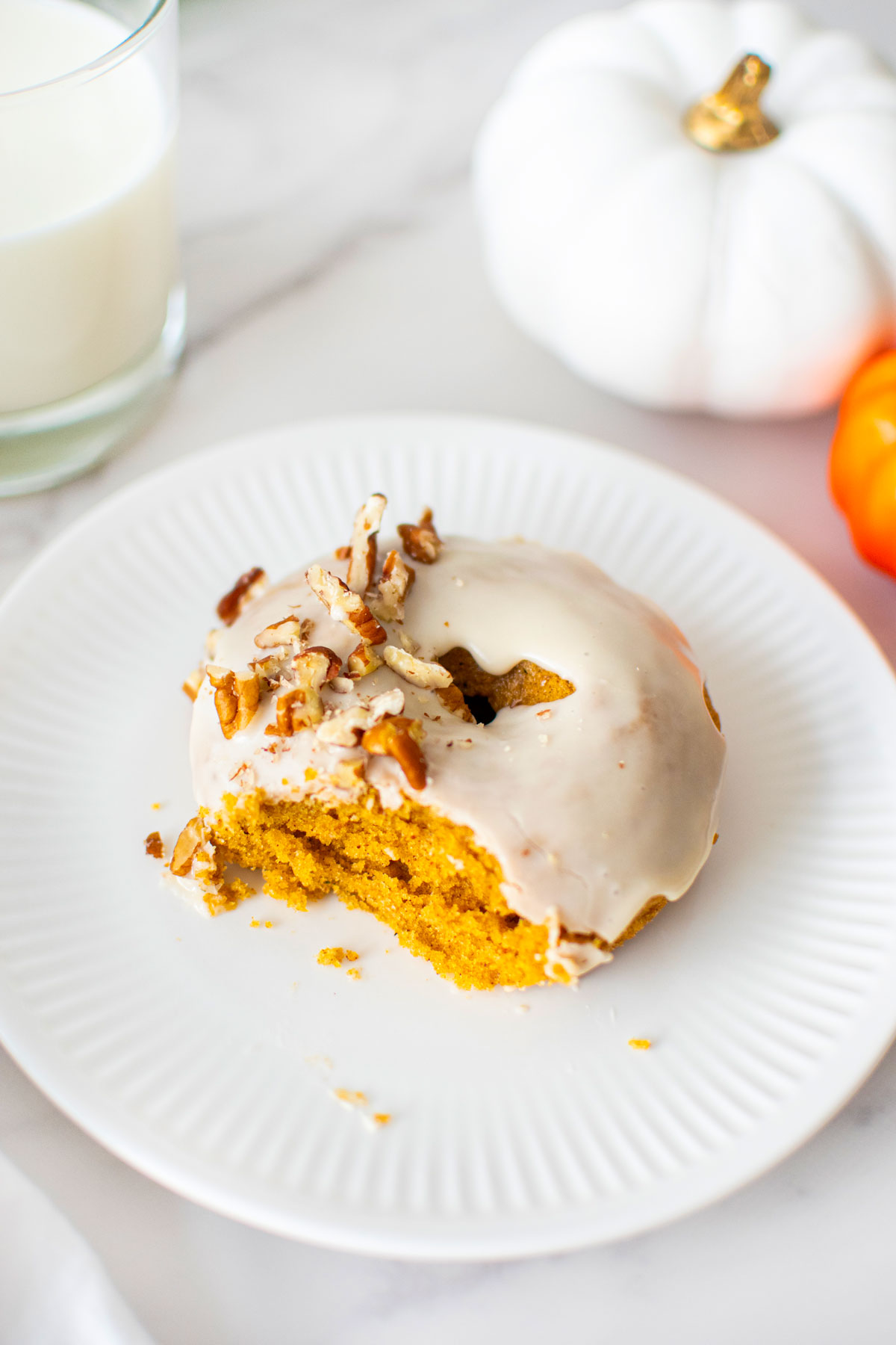 maple pumpkin spice donut with a bite taken out on a white plate on a white marble counter.