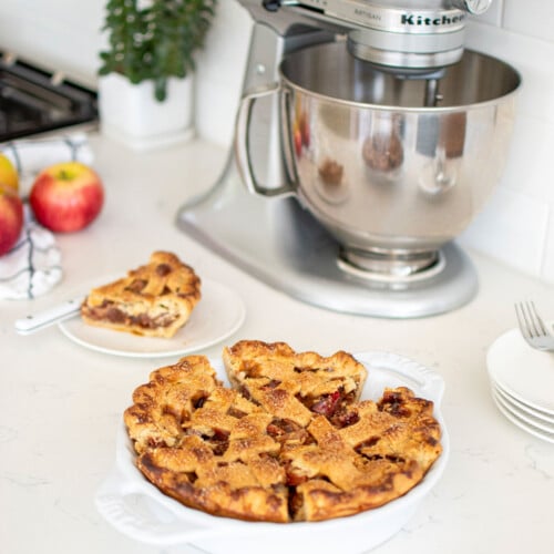 lattice apple pie on a white marble counter with a stand mixer.