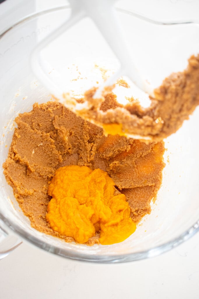 creamed butter and sugar with pumpkin in a glass mixing bowl on a marble counter.