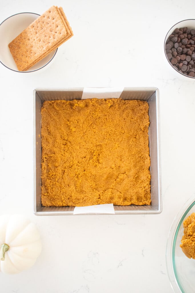 pumpkin spice smore bar dough in a baking pan on a white marble counter.