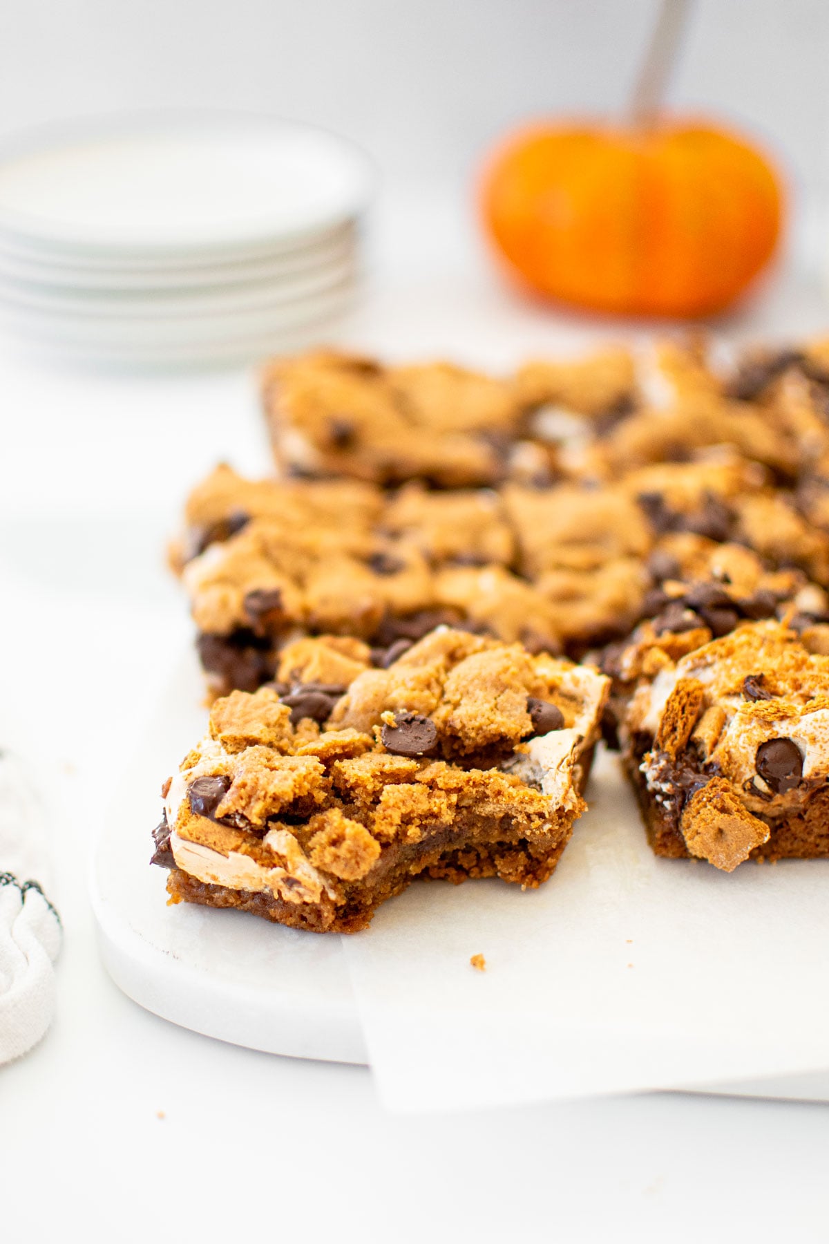 pumpkin spice smore bars cut into squares on a white marble counter with pumpkins.