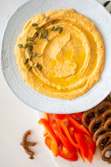 roasted red pepper hummus with purple garlic in a bowl on a charcuterie platter on a white marble table.
