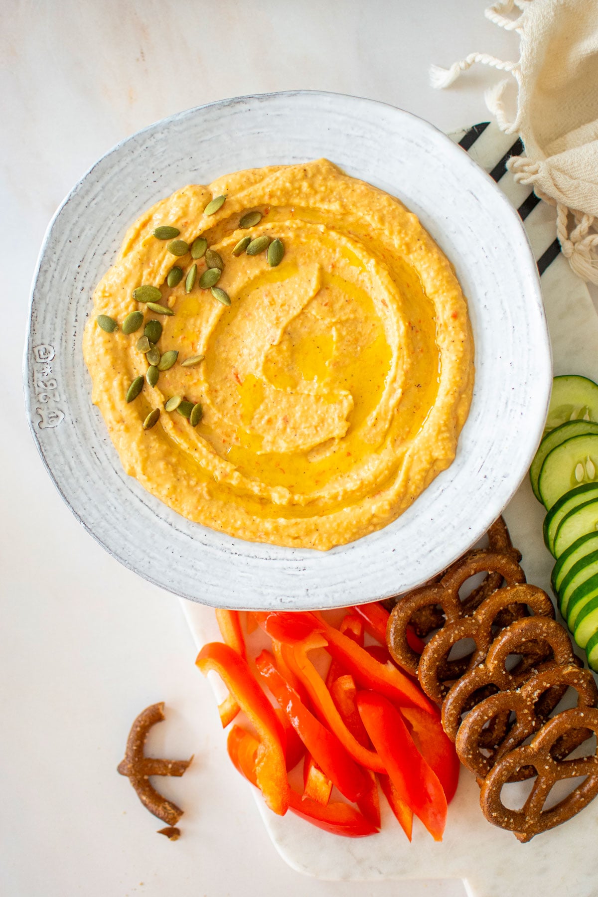 roasted red pepper hummus with purple garlic in a bowl on a charcuterie platter on a white marble table.