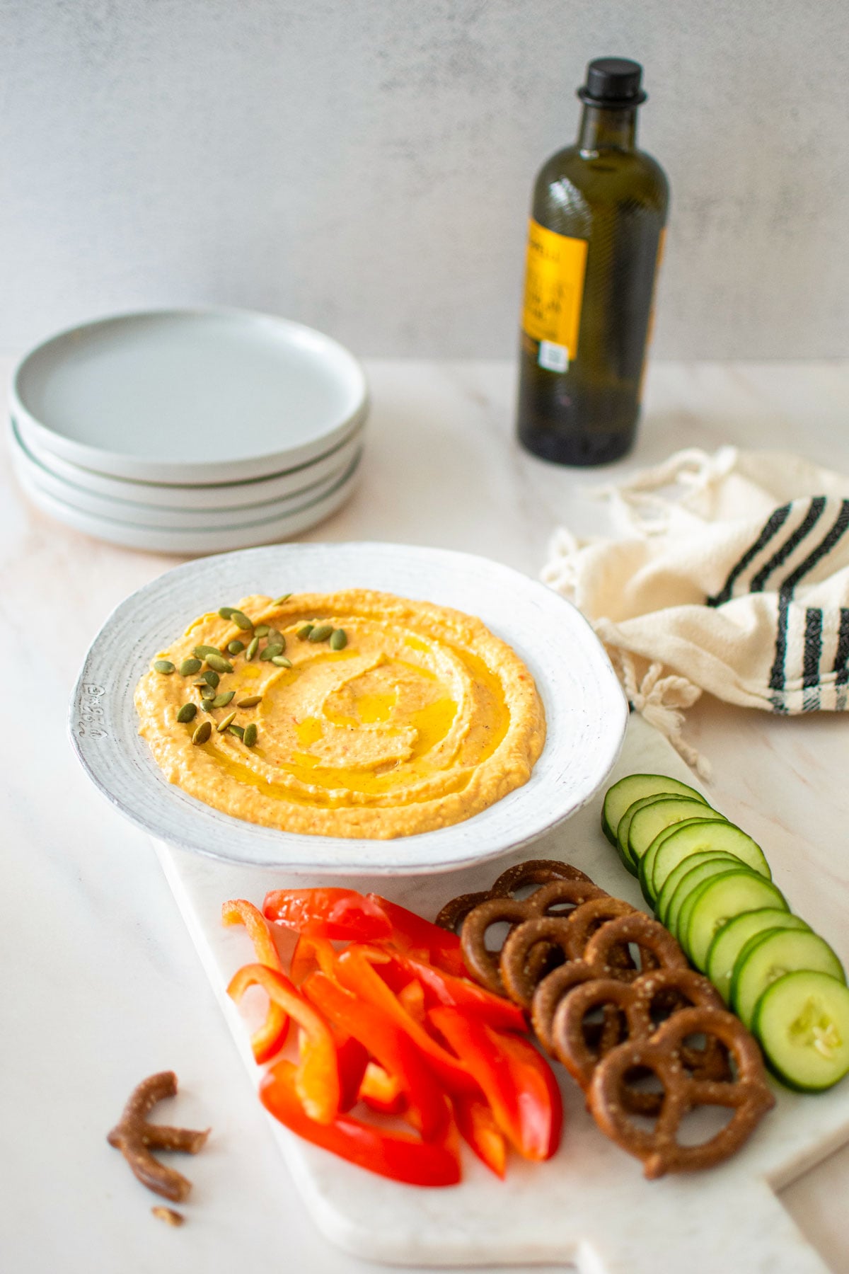 roasted red pepper hummus with purple garlic in a bowl on a charcuterie platter on a white marble table.