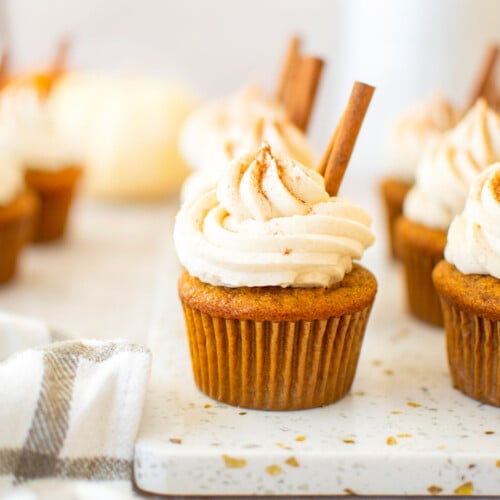 sourdough pumpkin spice cupcakes with cinnamon sticks on a marble board with pumpkins in the background.