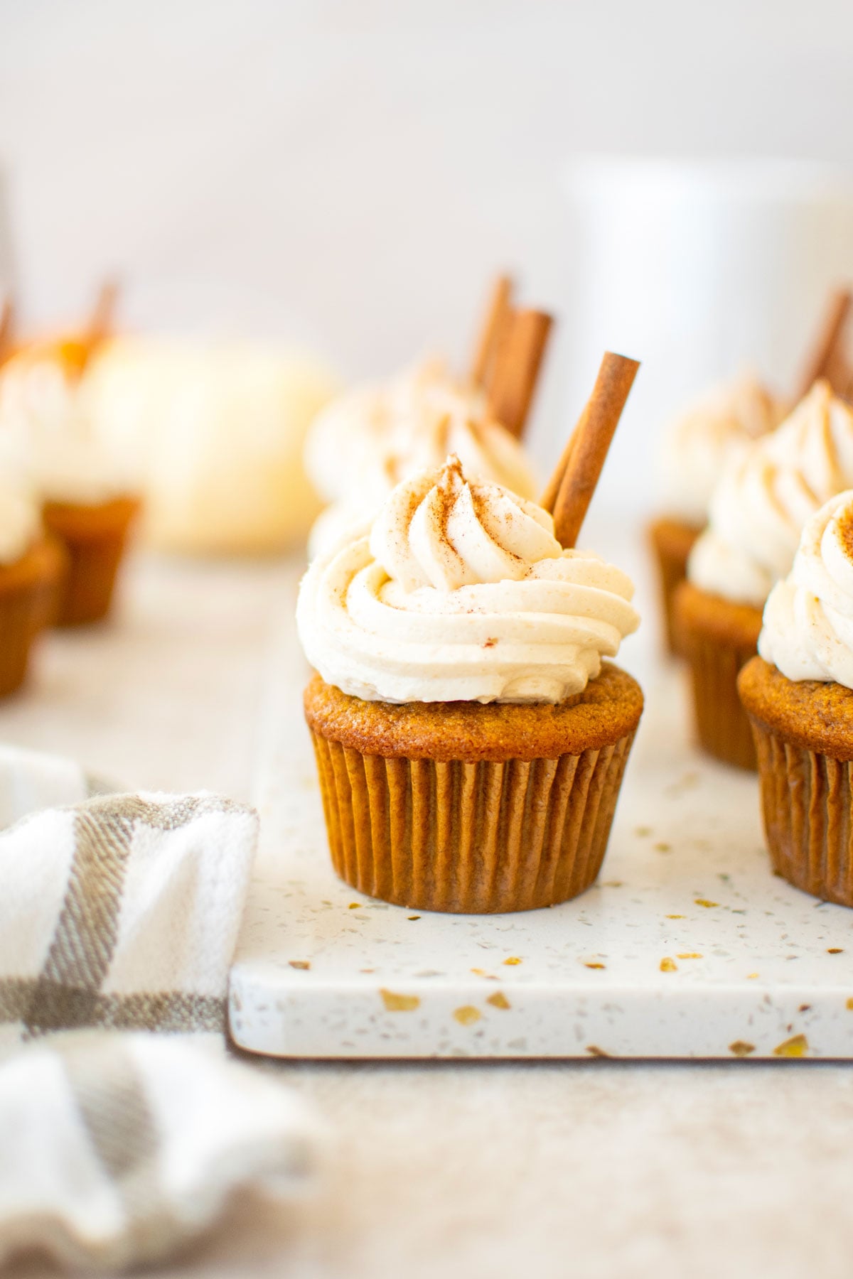 sourdough pumpkin spice cupcakes with cinnamon sticks on a marble board with pumpkins in the background.