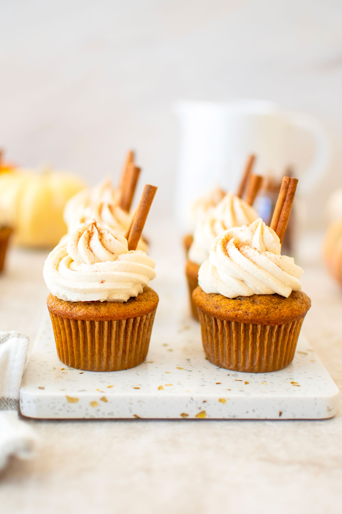 sourdough pumpkin spice cupcakes with cinnamon sticks on a marble board with pumpkins in the background.