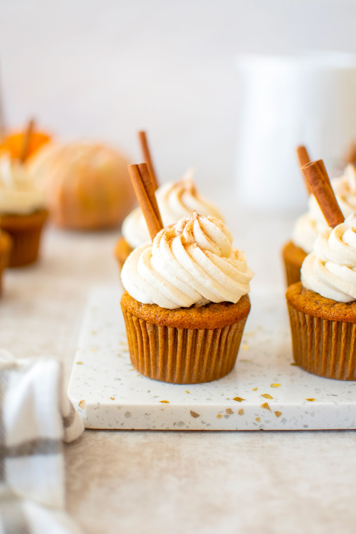 sourdough pumpkin spice cupcakes with cinnamon sticks on a marble board with pumpkins in the background.