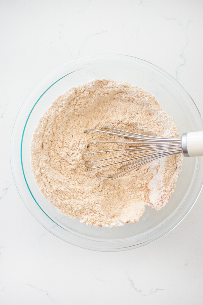 dry ingredients for sourdough pumpkin spice cupcakes in a glass mixing bowl with a whisk on a marble counter.