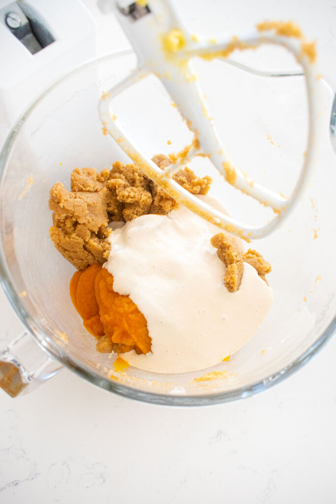 ingredients for sourdough pumpkin spice cupcakes in a glass mixing bowl on a white marble counter.