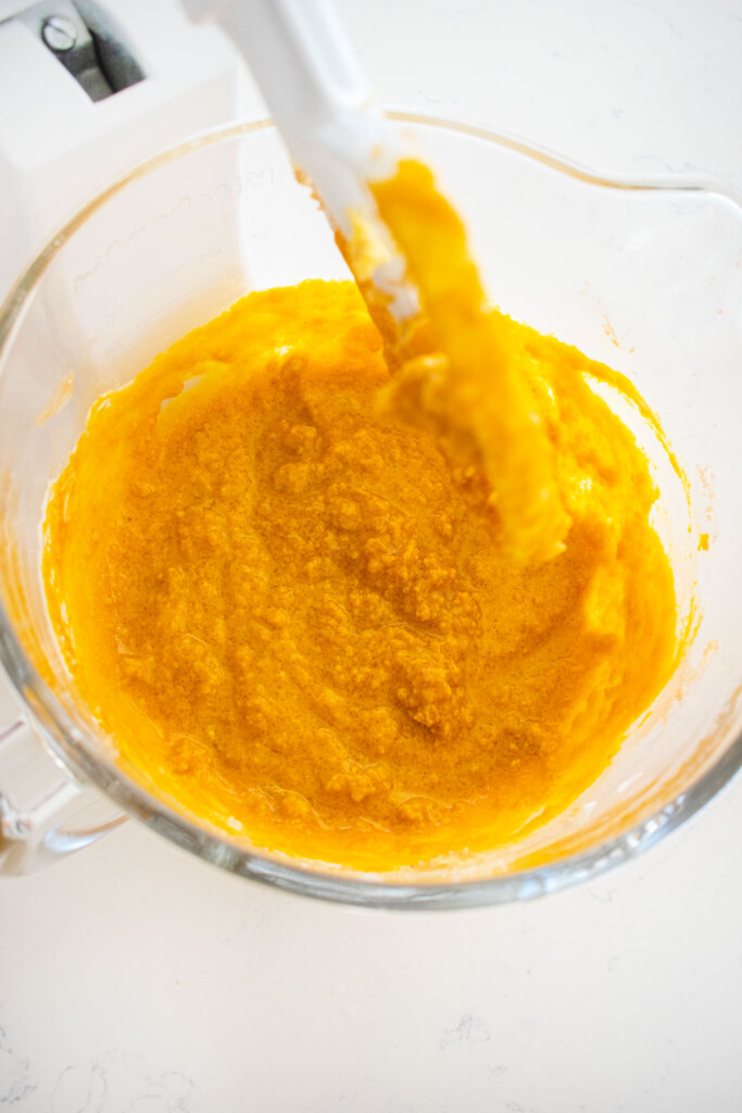 ingredients for sourdough pumpkin spice cupcakes in a glass mixing bowl on a white marble counter.