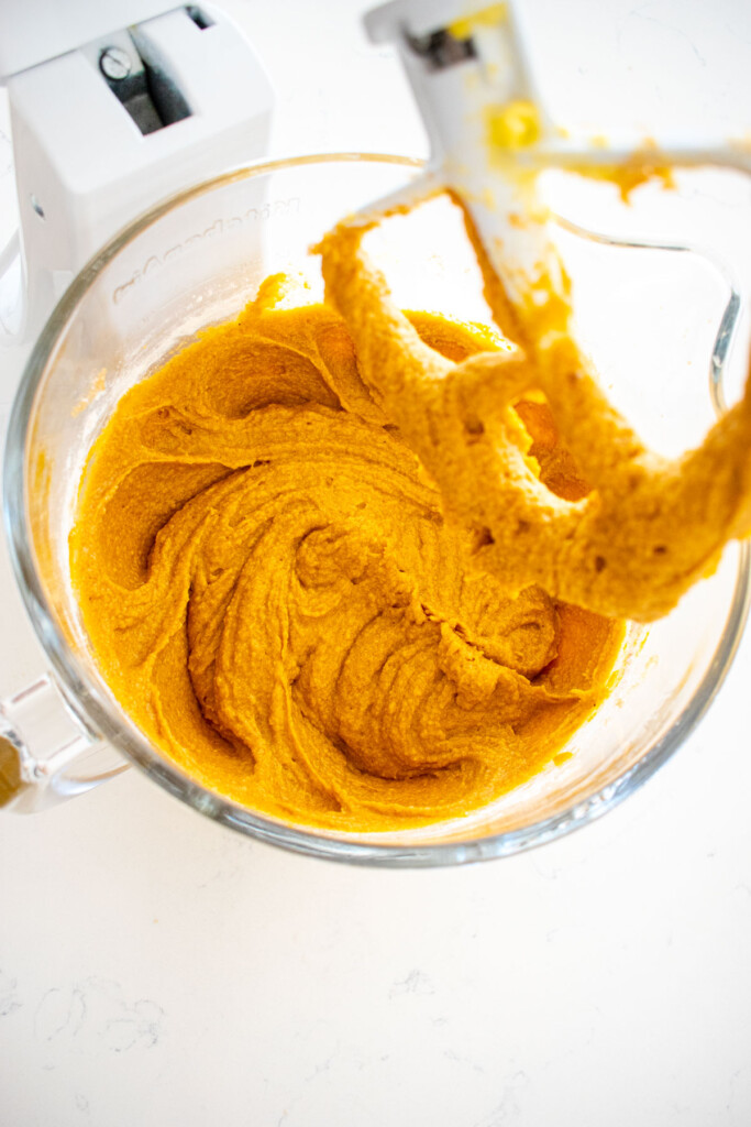 sourdough pumpkin spice cupcake batter in a glass mixing bowl on a white marble counter.