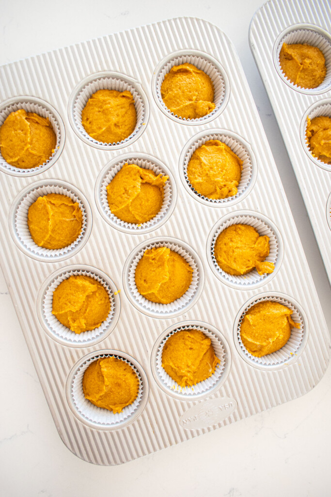 cupcake pans filled three quarters full of sourdough pumpkin spice cupcake batter on a white marble counter.