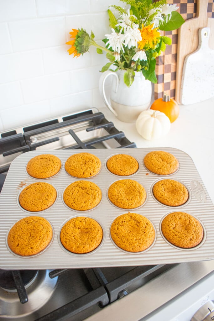 baked sourdough pumpkin spice cupcakes cooling in the cupcake pan on top of a stove.