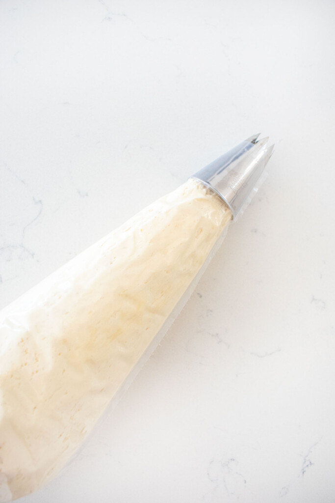 piping bag with a decorating tip with cream cheese frosting on a white marble counter.