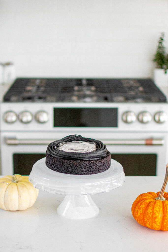 spooky rose cake being assembled on a cake stand on the kitchen counter with pumpkins.