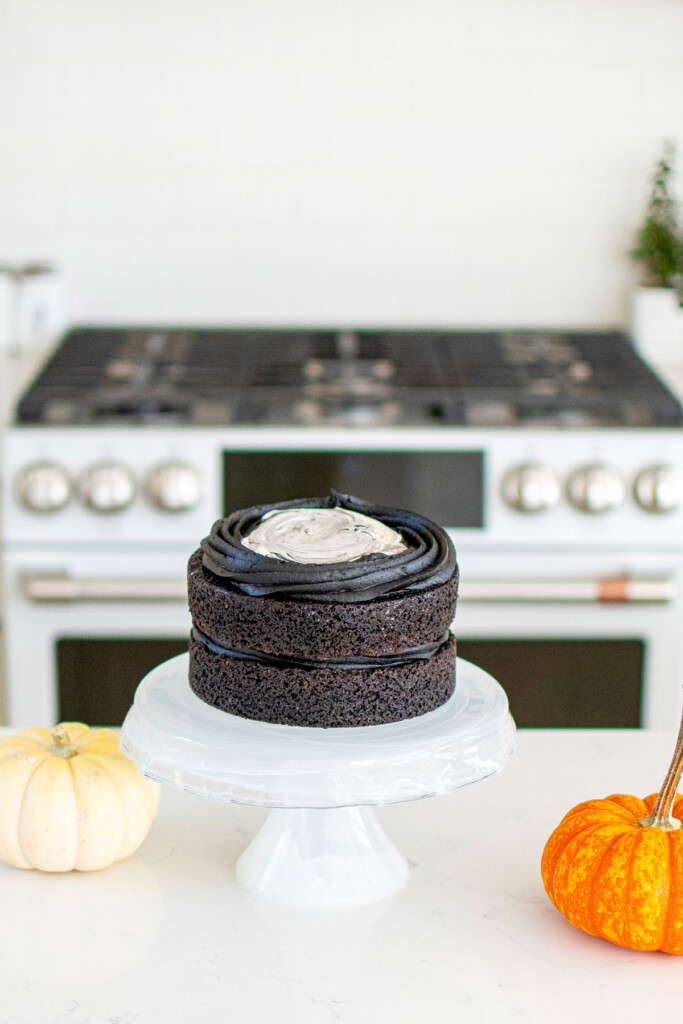 spooky rose cake being assembled on a cake stand on the kitchen counter with pumpkins.