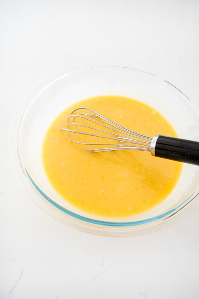 wet ingredients for spooky rose halloween cake in a glass mixing bowl on a marble counter with a whisk.