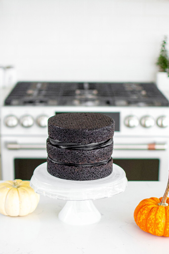 spooky rose cake being assembled on a cake stand on the kitchen counter with pumpkins.