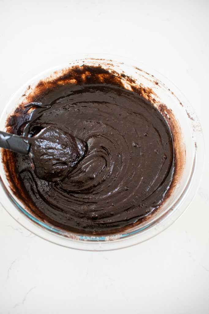 black chocolate cake batter in a glass mixing bowl on a marble counter.