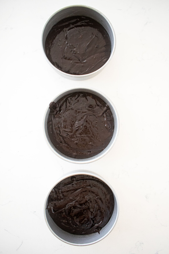 black chocolate cake batter in cake pans on a marble counter.