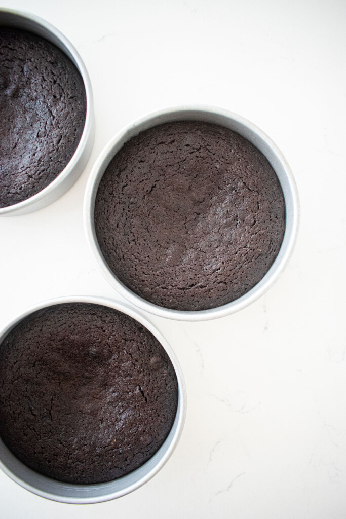 black chocolate cake in cake pans on a marble counter.