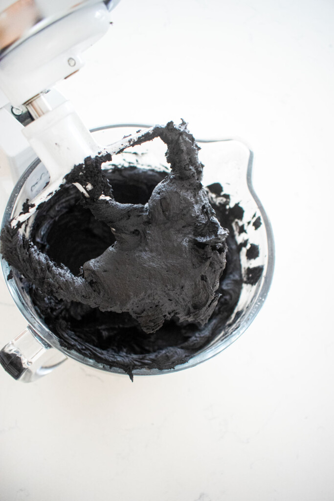 black buttercream frosting in a stand mixer on a white marble counter.