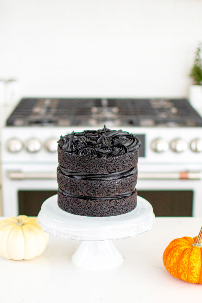 spooky rose cake being assembled on a cake stand on the kitchen counter with pumpkins.