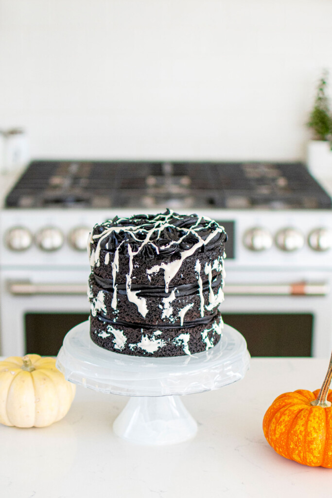 spooky rose cake being assembled on a cake stand on the kitchen counter with pumpkins.