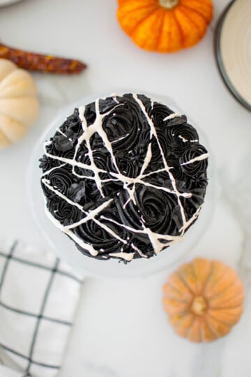 spooky rose cake for halloween on a cake stand on a white marble counter with pumpkins.
