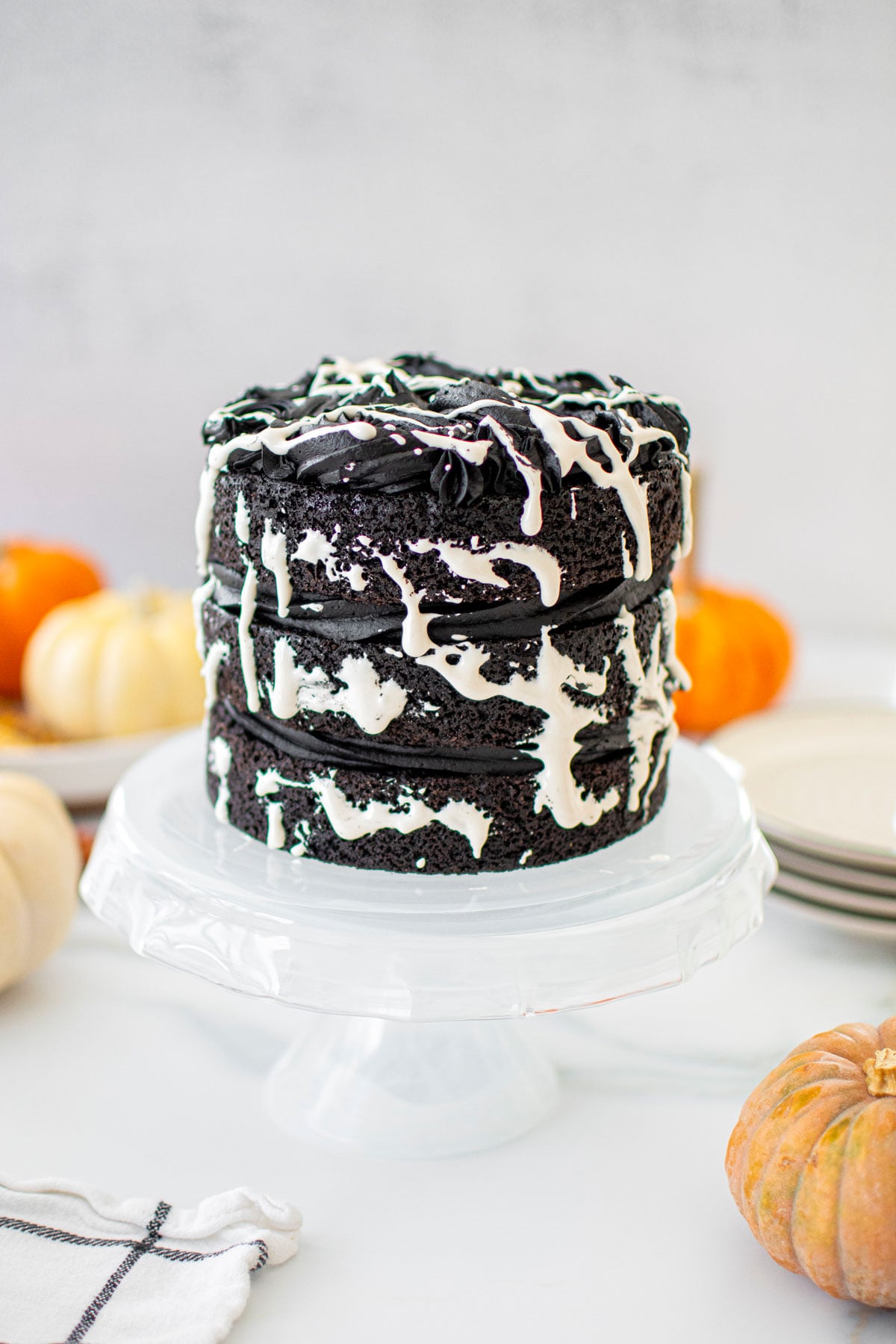 spooky rose cake for halloween on a cake stand on a white marble counter with pumpkins.