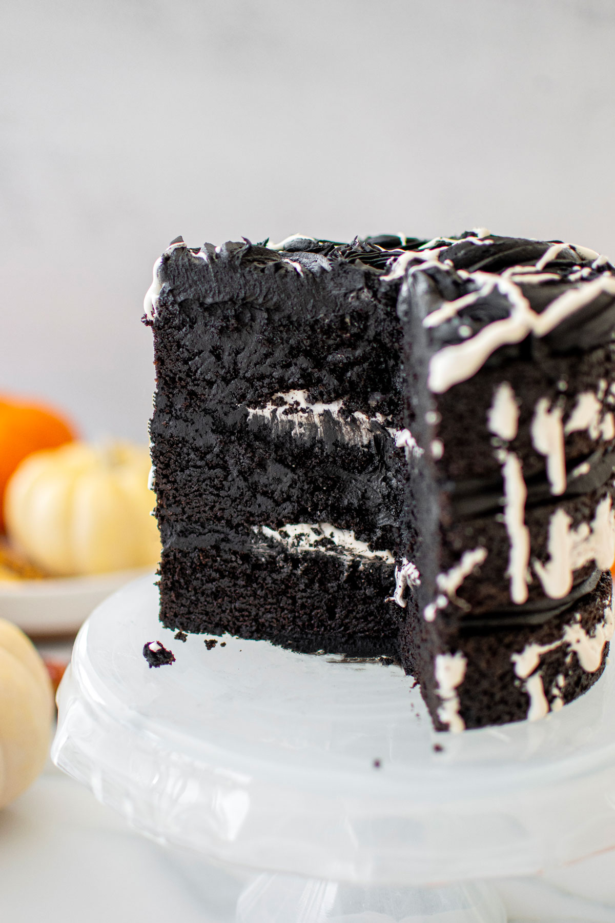 spooky rose cake for halloween cut into on a cake stand on a white marble counter with pumpkins.