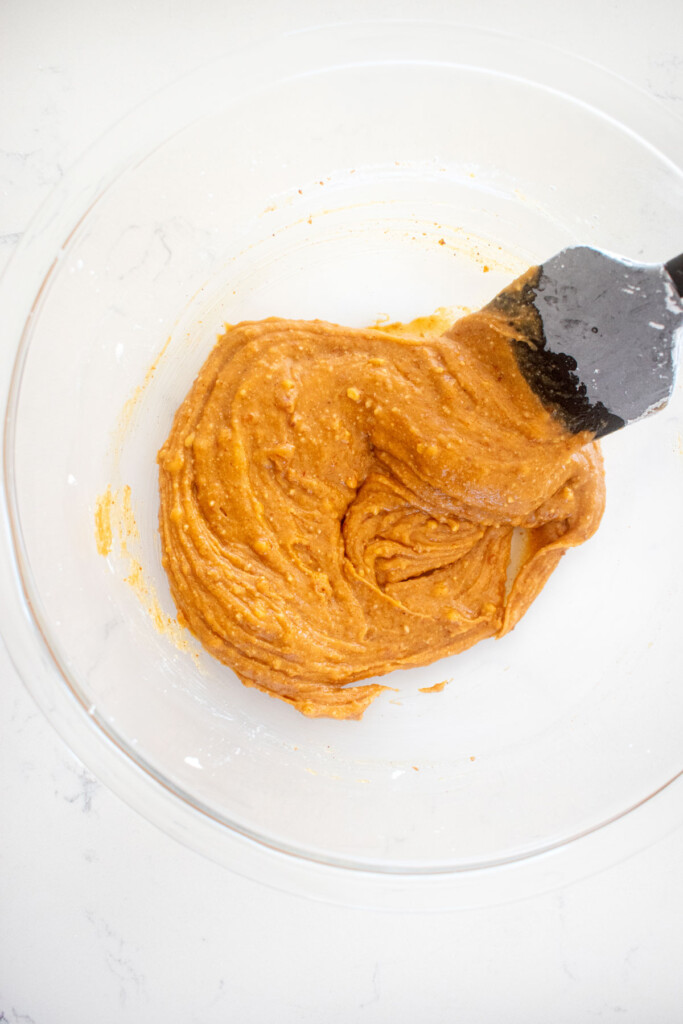 peanut butter filling in a glass mixing bowl with a spatula on a white marble counter.